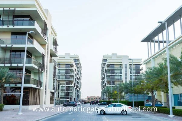 A street view of modern residential apartment buildings in Khalifa City, Abu Dhabi, with palm trees lining the road and cars parked in front.