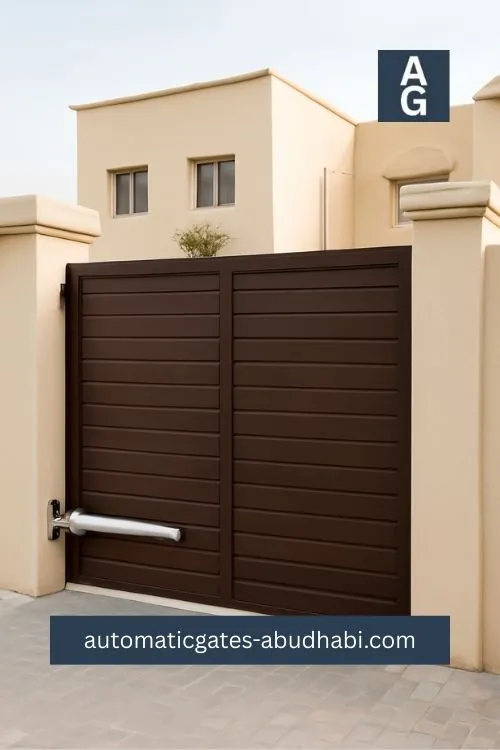 A sleek dark brown wooden automatic gate with a silver-colored opener installed in front of a minimalist beige residential home in Al Sadar