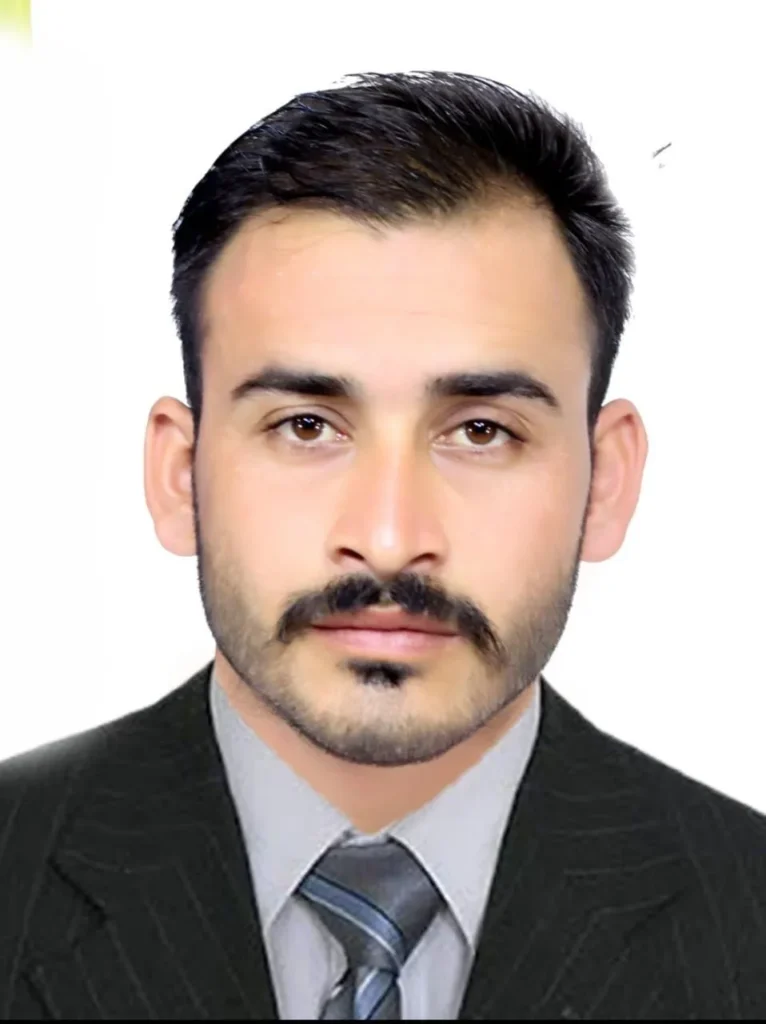 A man with a mustache wearing a formal dress shirt and tie, portrait taken from the shoulders up. He has a comb over hairstyle and is dressed in a blazer. His facial expression is neutral, and he has a well-groomed appearance, showcasing his jawline and cheek structure.